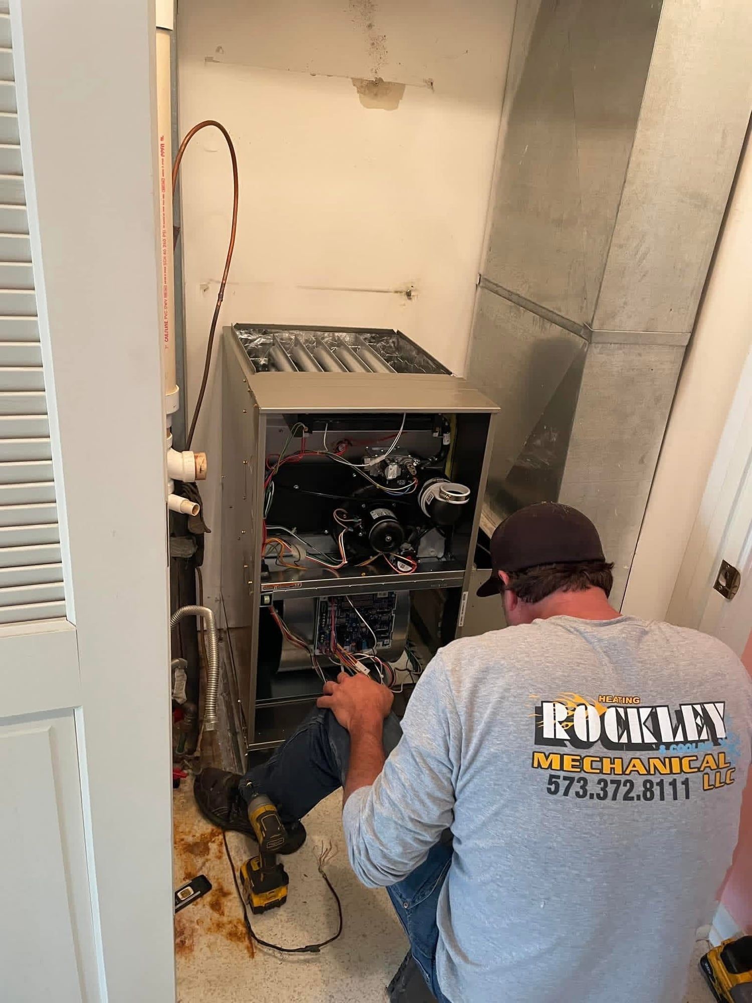 A Rockley Mechanical technician wiring a gas furnace with its panels off in a utility closet